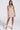 A woman poses in the RHODES TEXTURED MINI DRESS, a multicolor knit with a deep V-neckline and spaghetti straps, paired with platform heels adorned with large bows, set against a plain white background.