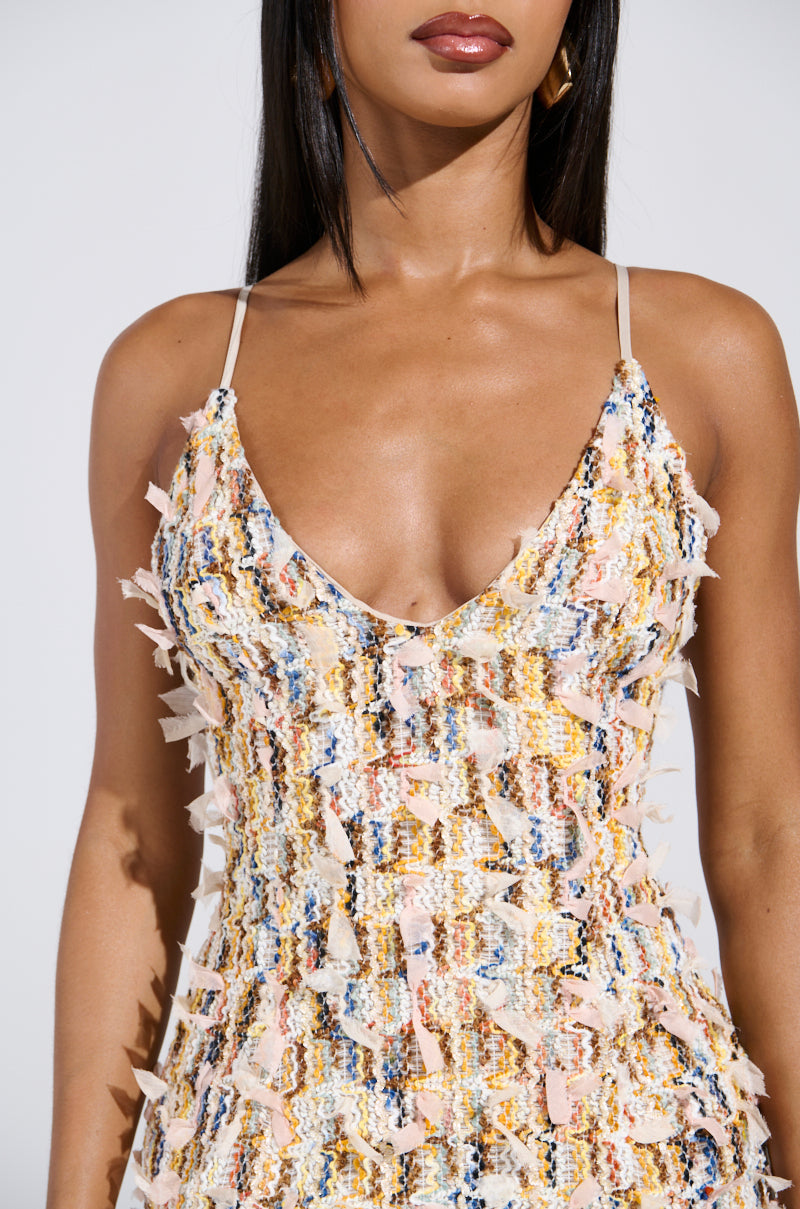 A woman wearing the RHODES TEXTURED MINI DRESS, a multicolored knit mini dress with a frayed pattern and V-neckline with thin straps, stands against a white background. Her long straight hair falls over her shoulders.