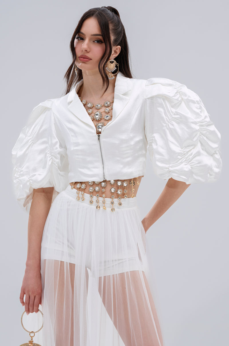 A woman in the HERE FOR A GOOD TIME RUFFLE SLEEVE BLAZER stands against a neutral background, showcasing its chic ruffle sleeves and cropped silhouette.