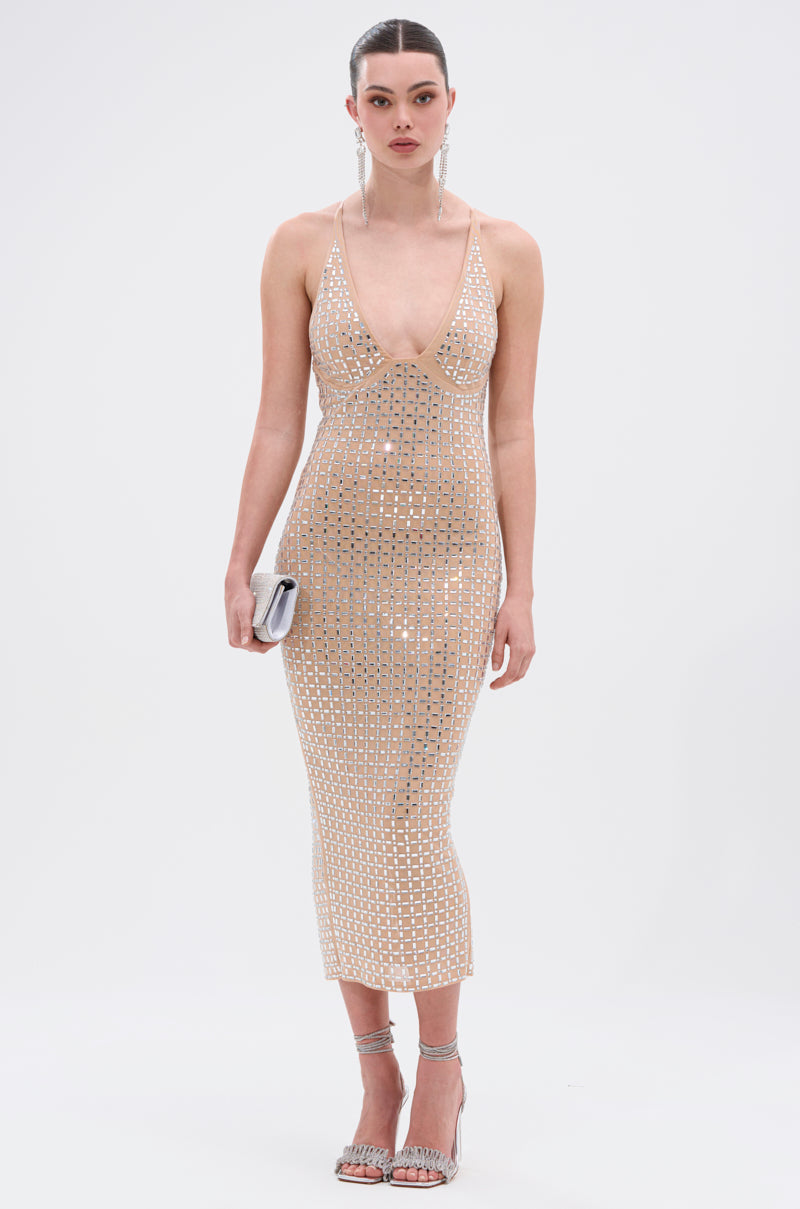 A woman poses against a plain white background in the QUEEN OF EVERYTHING MIDI DRESS—a fitted, nude, sleeveless mesh dress with mirrored embellishments—styled with silver heels and a metallic clutch. 0