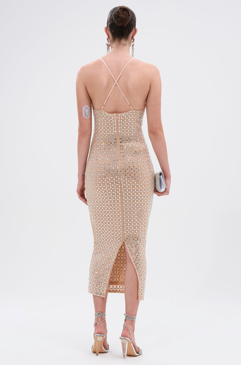 A person faces away, wearing the QUEEN OF EVERYTHING MIDI DRESS—nude mesh with geometric cutouts. Strappy heels, a small clutch, and a visible medical device on their upper arm complete the outfit. 5