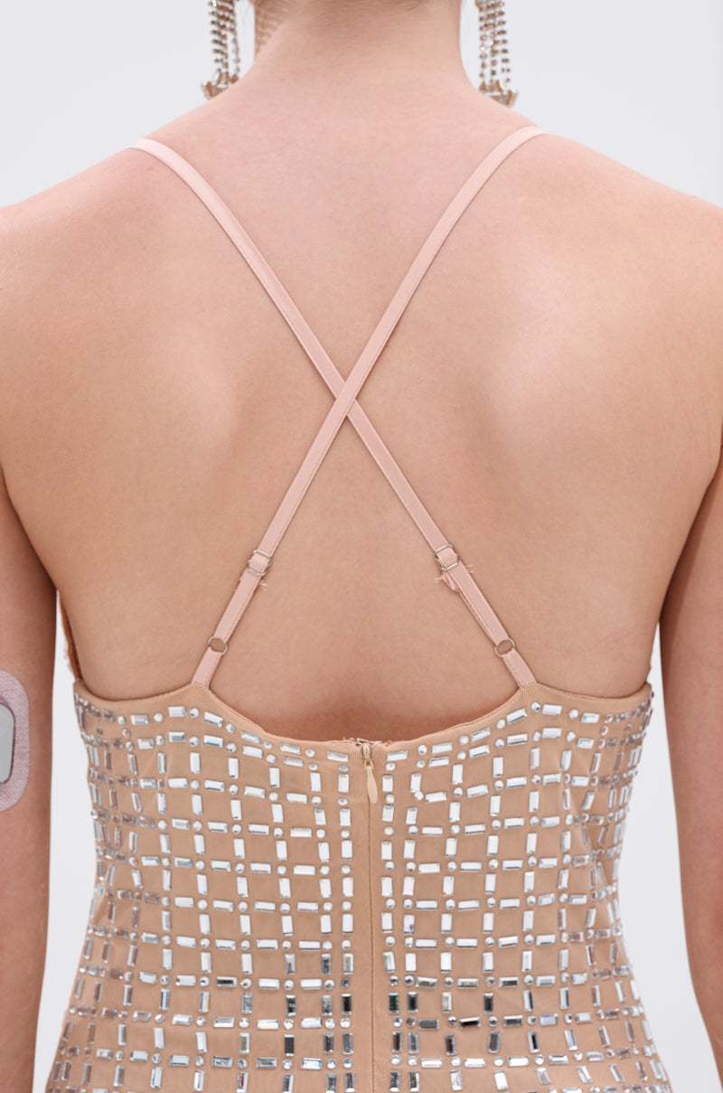 A close-up shows a person’s back wearing the QUEEN OF EVERYTHING MIDI DRESS with thin crisscross straps and mirrored embellishments. A medical device is on their upper left arm, and long earrings are partially visible. 7