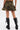 A person stands facing away, wearing the DARIA STUDDED CAMO MINI SKIRT and black knee-high boots with zippers and laces. Their hands rest on the skirt’s sides, showing tattoos above the backs of their knees.