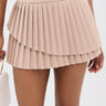 A person in the POETRY IN MOTION pleated mini skirt and a white crop top holds a cream handbag against a plain light gray background.