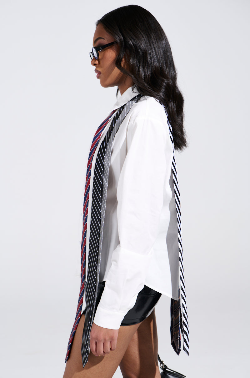 Wearing the OH J SPECIAL TIE TOP, a person with long hair and sunglasses saunters in a white shirt and leather shorts, exuding a longline silhouette. Colorful cascading ties against the plain background accent their style.