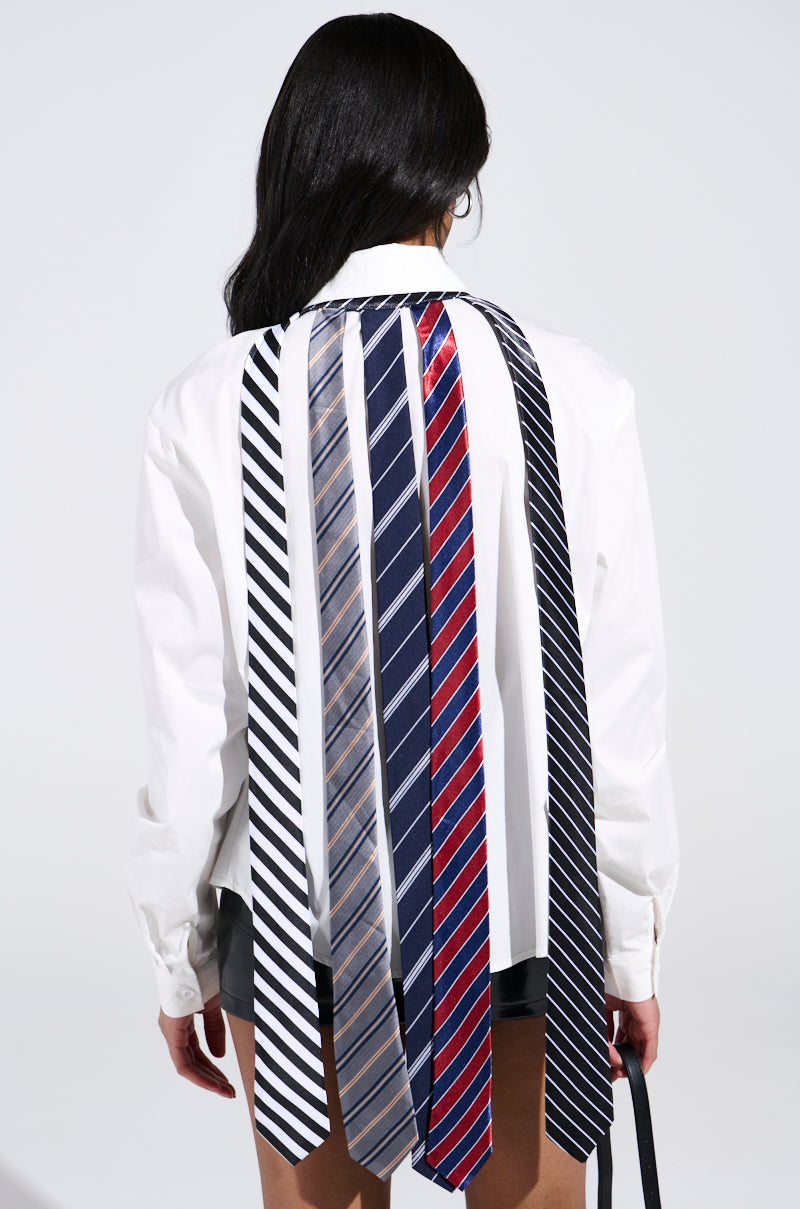 Wearing the OH J SPECIAL TIE TOP, a person in a white long-sleeve shirt stands with their back to the camera. The top features striking, cascading ties over the shoulders with unique colors and patterns, creating a vibrant longline silhouette against the plain shirt.