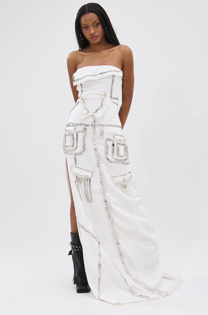 A woman poses against a plain white background in the COVER STAR DENIM MAXI DRESS, a strapless gown with metallic trim, pocket-like embellishments, and a thigh-high slit. She completes the look with black heeled boots and long straight hair.