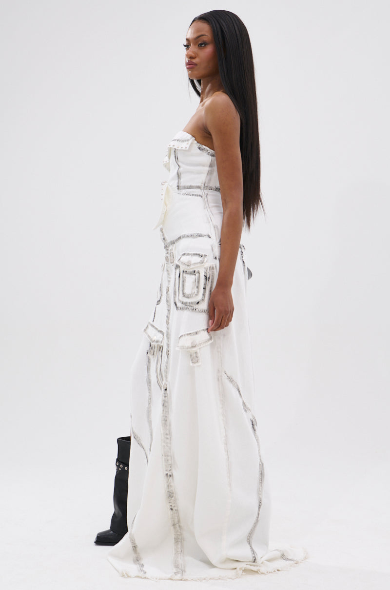 A woman with long straight hair wears the COVER STAR DENIM MAXI DRESS, a white, strapless floor-length piece with gray stitching and multiple pockets. She pairs it with black boots while standing against a plain white background.