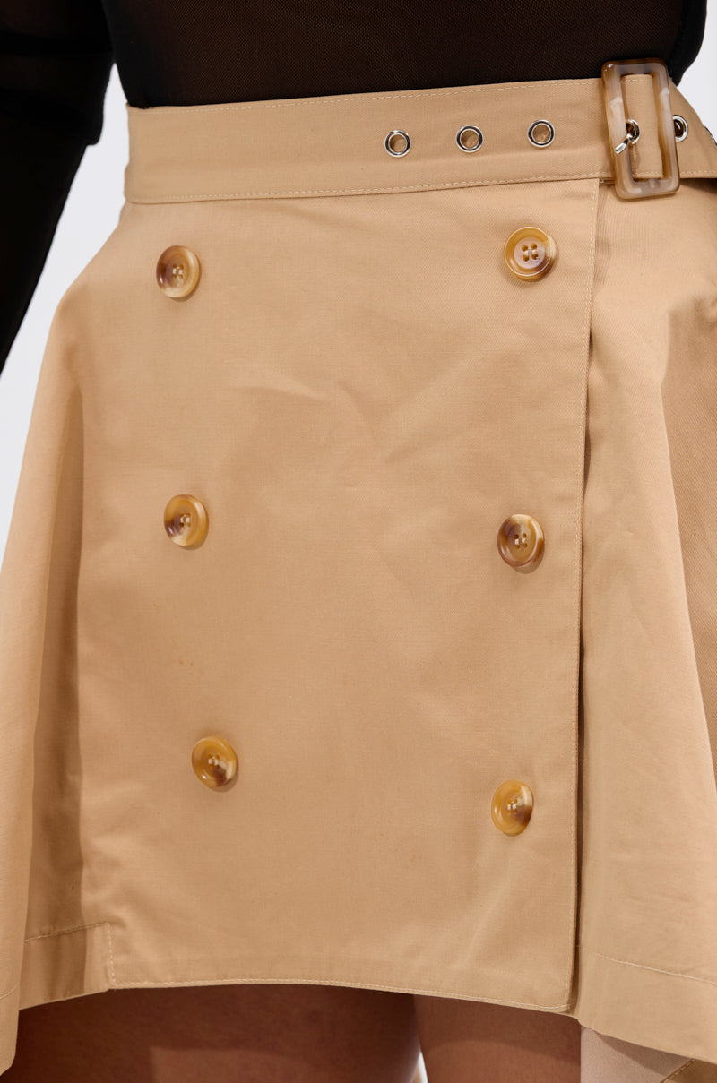 A close-up of the MAEVE MINI SKIRT: a tan mini skirt featuring large brown buttons in two vertical rows, a matching high-rise belt, and subtly flared structured fabric at the hem.