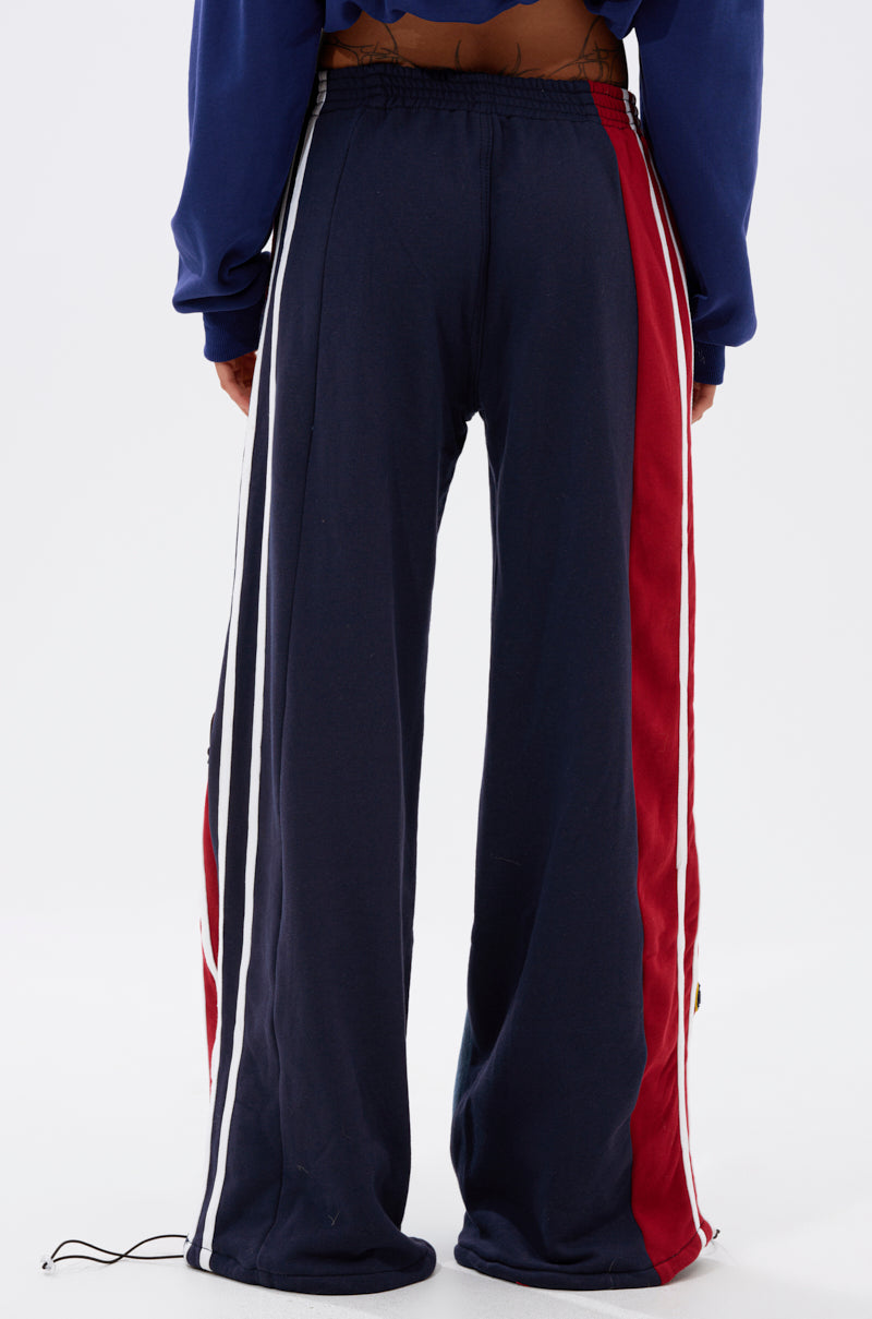 Person stands with their back to the camera, wearing LIGHTS OUT TWO-IN-ONE JEANS in navy blue with red side panels and white stripes, paired with a blue long-sleeve top.