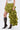Wearing a white sleeveless top, the CLAIRE HIGH LOW RUFFLE SKIRT in olive green with long layered sides, and knee-high black lace-up heeled boots, a person stands against a plain background.