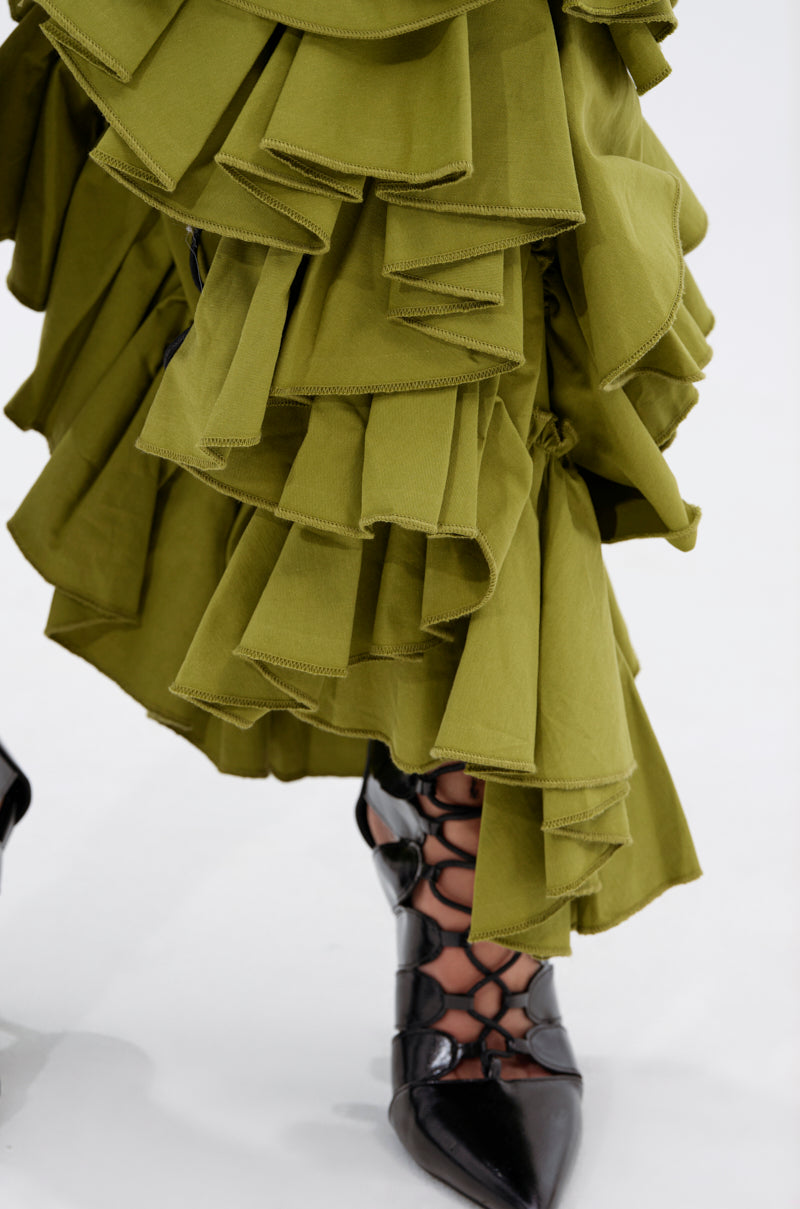 Close-up of the CLAIRE HIGH LOW RUFFLE SKIRT in layered olive green, paired with black pointed-toe lace-up shoes, on a white background.