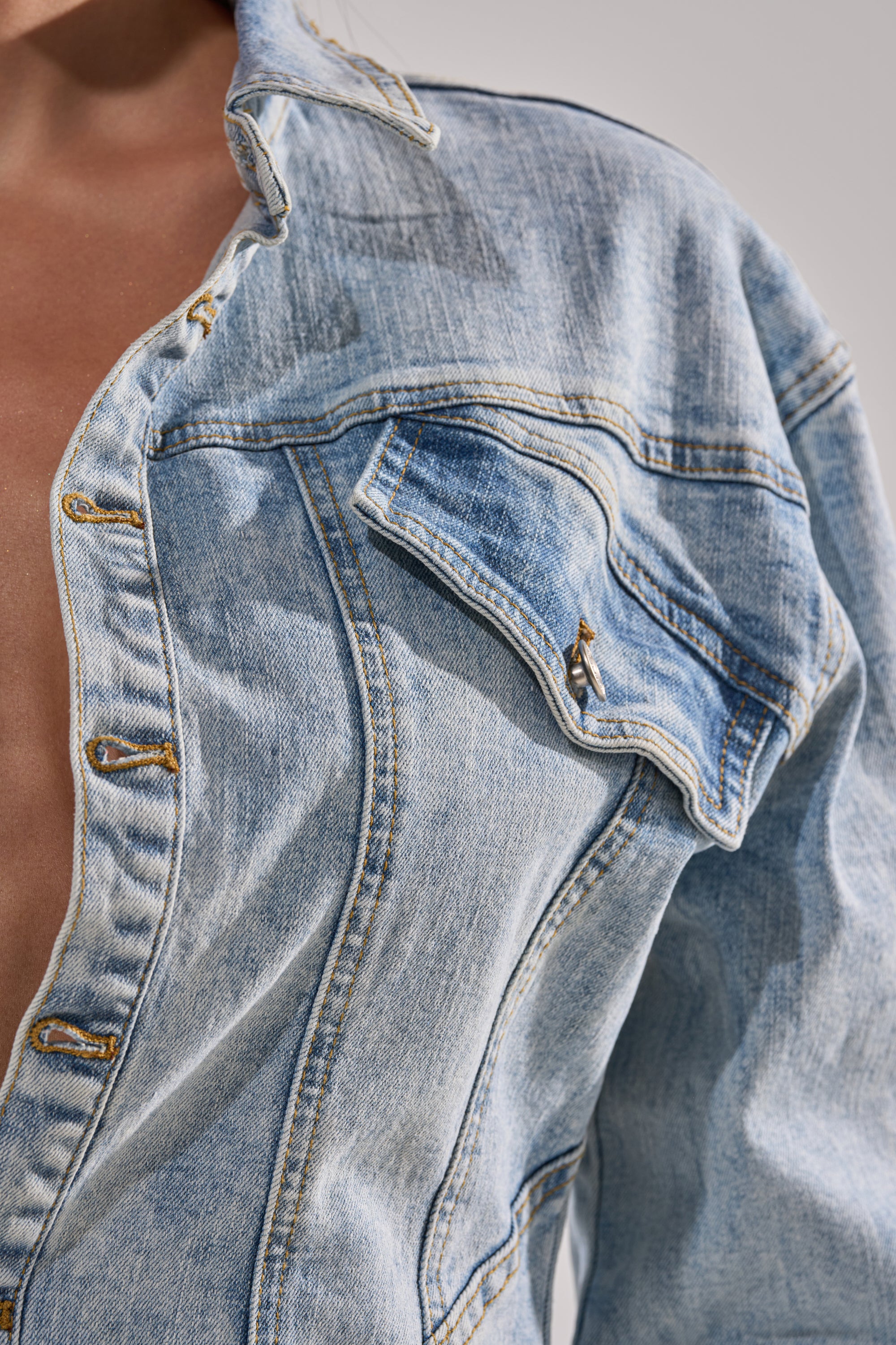 Close-up of a person wearing the DENIM FOR DAYS MAXI DRESS, featuring light-wash denim, metal buttons, and a flap chest pocket. The dress is slightly open at the front, set against a plain, neutral background.