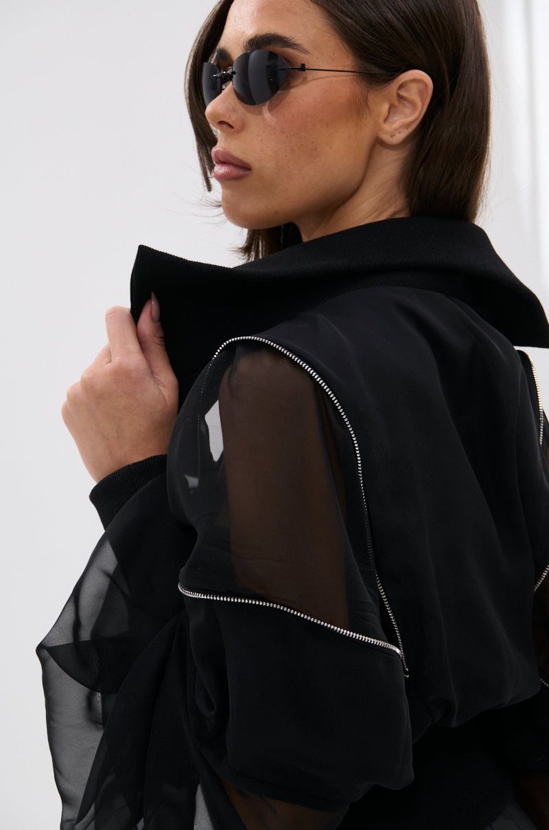 Woman wearing CHOOSE YOUR FIGHTER MESH INSERT BOMBER with zippered details and black sunglasses, holding the collar up and looking to the side. Her elevated street-style look pops against a plain, light background. 12