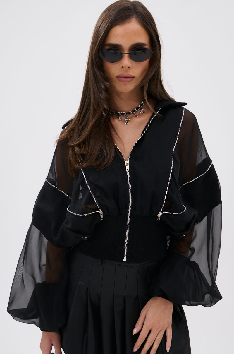 A woman with long brown hair exudes elevated street style in black sunglasses, a CHOOSE YOUR FIGHTER MESH INSERT BOMBER with white piping, a black pleated skirt, and a silver choker necklace as she stands against a plain white background. 4