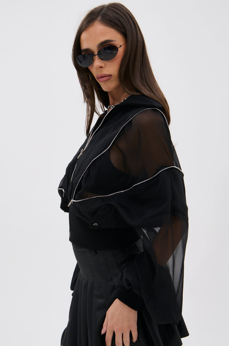 A woman with long brown hair and black sunglasses wears the CHOOSE YOUR FIGHTER MESH INSERT BOMBER styled with a pleated black skirt, standing against a plain white background. 6