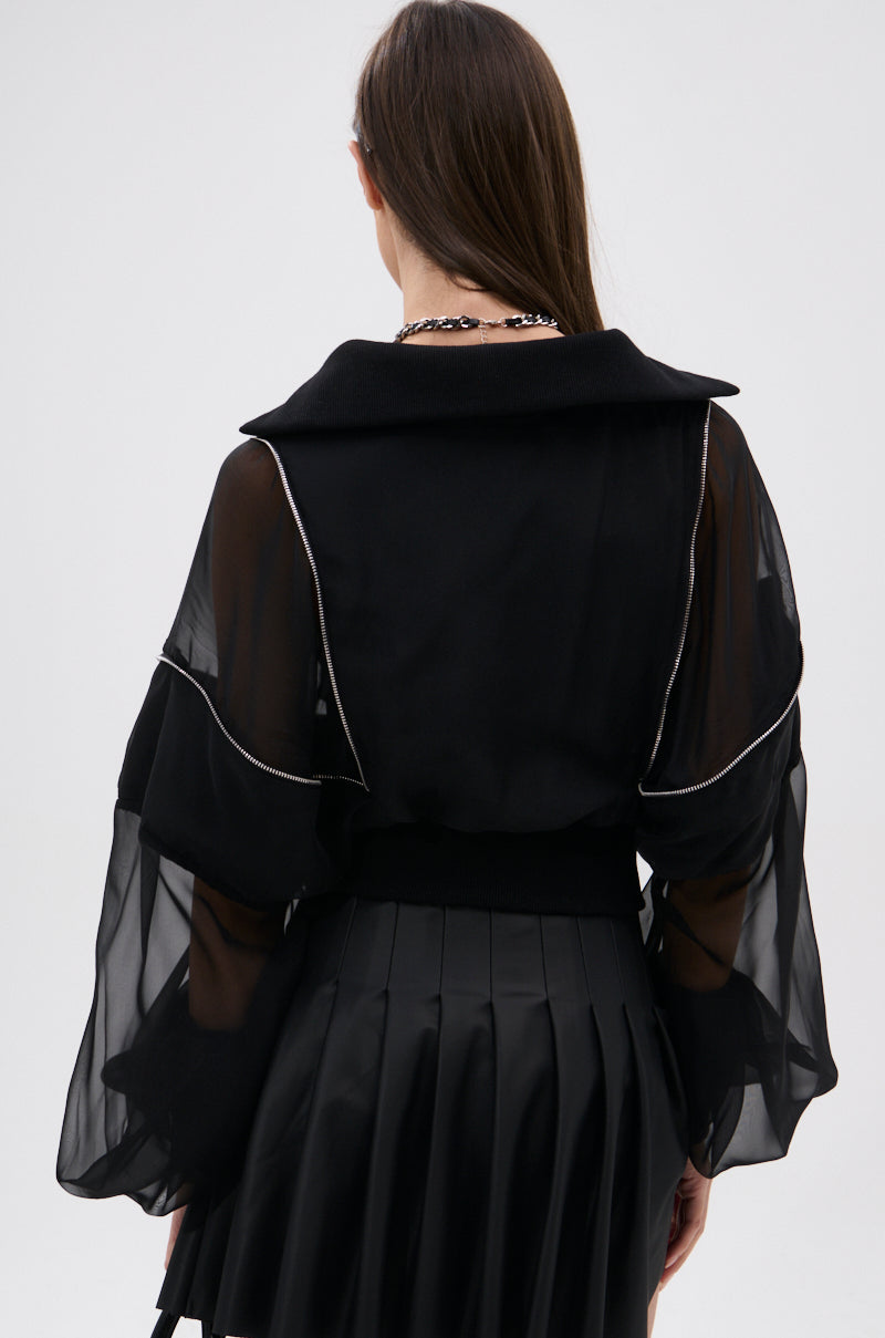 A woman with long brown hair, shown from the back against a plain light background, wears the CHOOSE YOUR FIGHTER MESH INSERT BOMBER styled with a pleated black skirt. 7