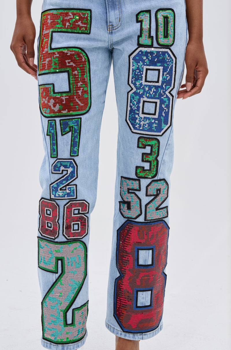 Wearing the CHAMPION GRAPHIC DENIM PANT, featuring light blue denim and bold, multicolored embroidered numbers for vintage varsity flair and playful street-style energy.
