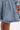 A close-up shows a person in the FELT CUTE SWEATSHIRT DENIM MINI DRESS, featuring a skater silhouette. Their manicured hand rests by the hem, subtly revealing an upper thigh tattoo against a plain white backdrop.