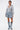 A woman poses against a white background wearing the FELT CUTE SWEATSHIRT DENIM MINI DRESS. She sports wet-look hair, visible tattoos, and completes her streetwear-inspired look with knee-high denim boots with white laces.