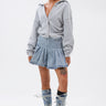 A woman poses against a white background wearing the FELT CUTE SWEATSHIRT DENIM MINI DRESS. She sports wet-look hair, visible tattoos, and completes her streetwear-inspired look with knee-high denim boots with white laces.