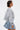 A woman with short, slicked-back hair models the FELT CUTE SWEATSHIRT DENIM MINI DRESS in a relaxed streetwear style, standing in profile against a plain white background.