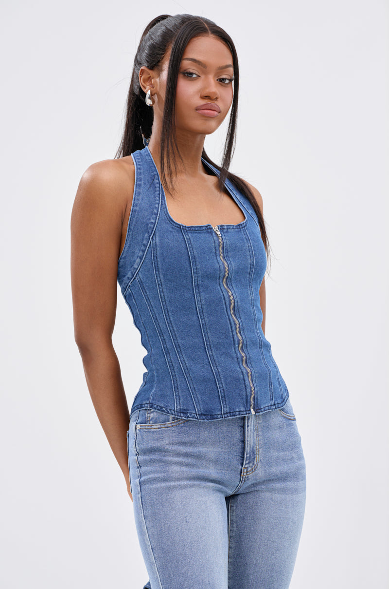 A woman stands confidently against a white background, wearing the CALM AND COLLECTED CORSET TOP— a sleeveless, square-neck dark-wash denim top with front seams—paired with light blue jeans.