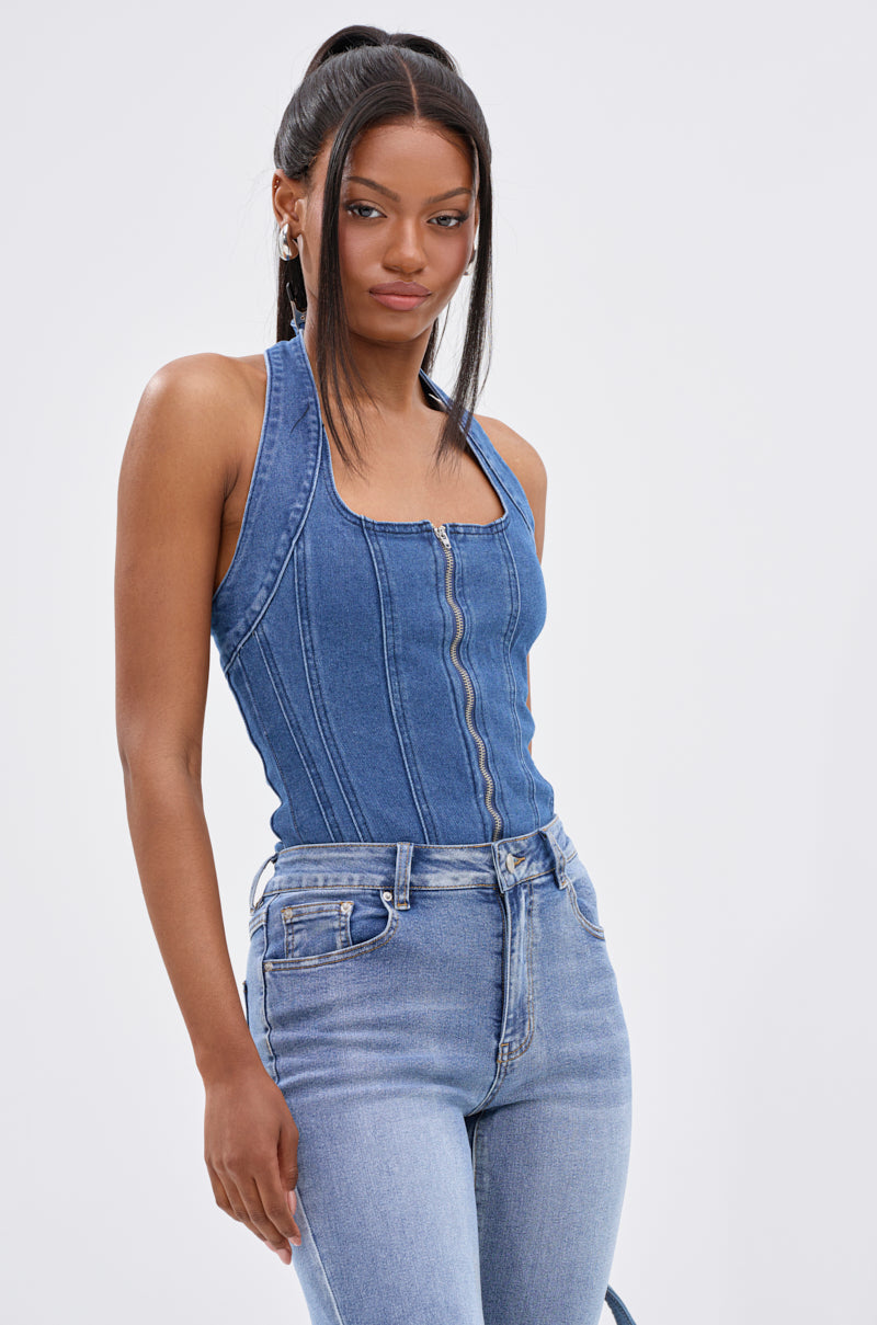 A woman with long dark hair wears the CALM AND COLLECTED CORSET TOP in a dark-wash denim style and high-waisted light blue jeans, standing against a plain light background.