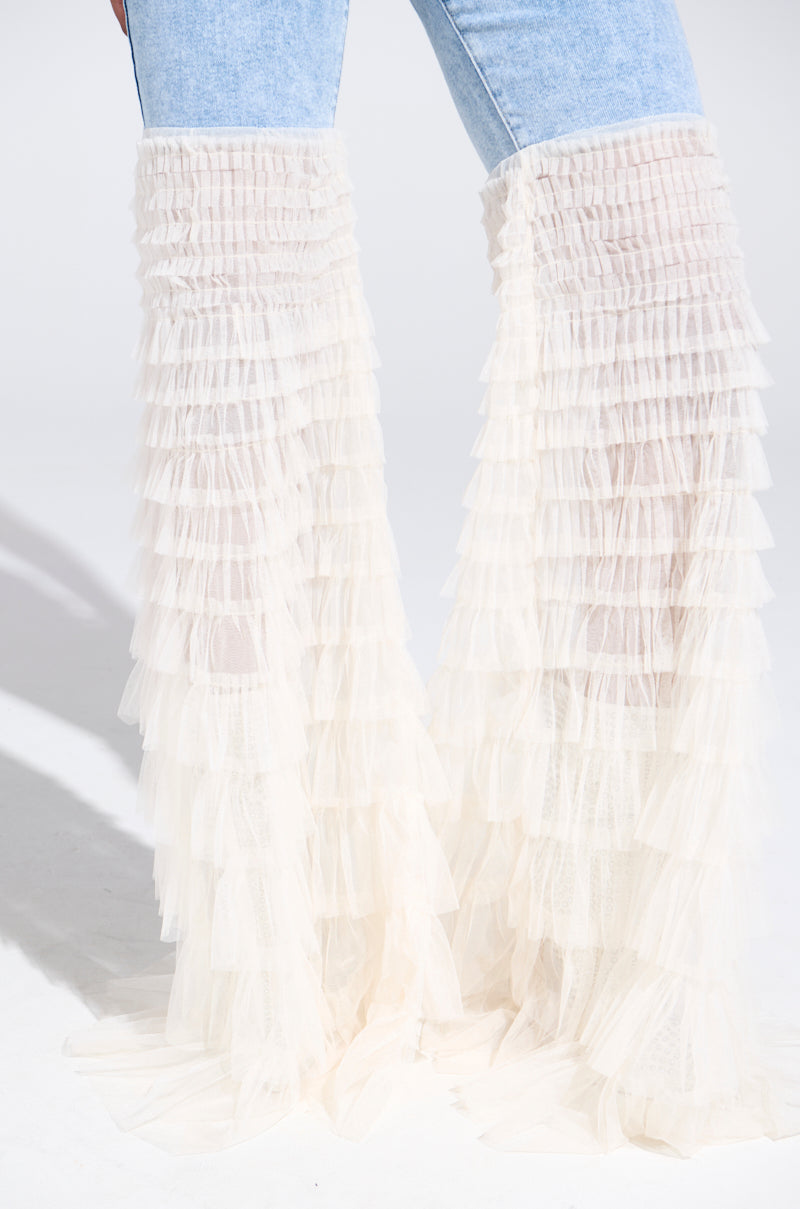 A close-up shows a person wearing the "LOOK AT ME GO DENIM PANT WITH RUFFLE BOTTOM" featuring light blue denim and sheer tulle embellishments that cascade into a dramatic flared leg silhouette from the knees, set against a plain white background.