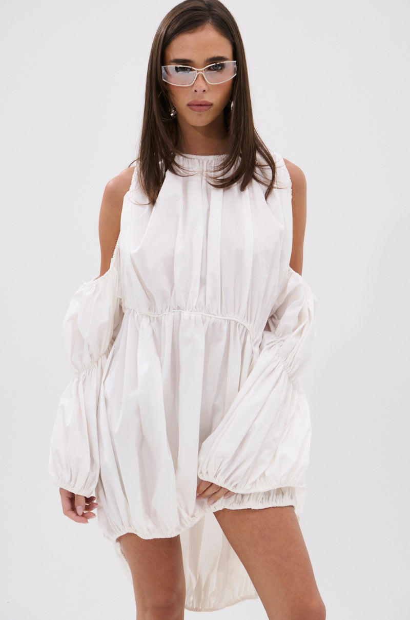 A woman in clear glasses wears the INSTA SAW IT FIRST ADJUSTABLE MINI DRESS, featuring puffy sleeves and cold-shoulder cutouts, standing against a plain white background and looking at the camera.