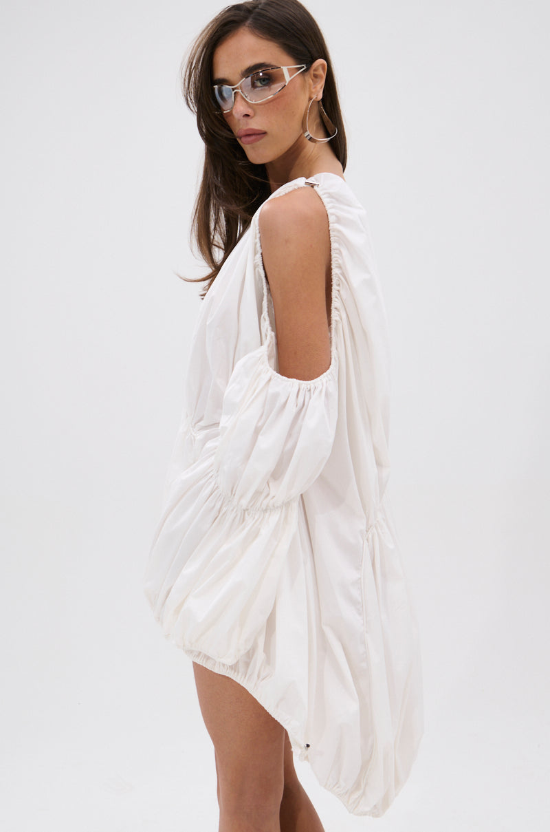 A woman with long brown hair wears angular clear glasses, large hoop earrings, and the INSTA SAW IT FIRST ADJUSTABLE MINI DRESS, posing against a plain white background.