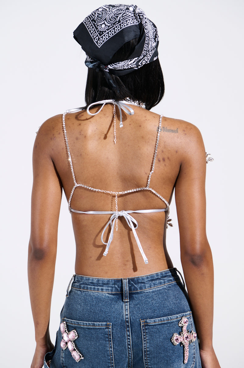 Rear view of a person wearing the BLINDED BY THE LIGHTS RHINESTONE TOP and jeans with floral-inspired rhinestone pockets. Their back is visible, highlighting the unique decorative details.