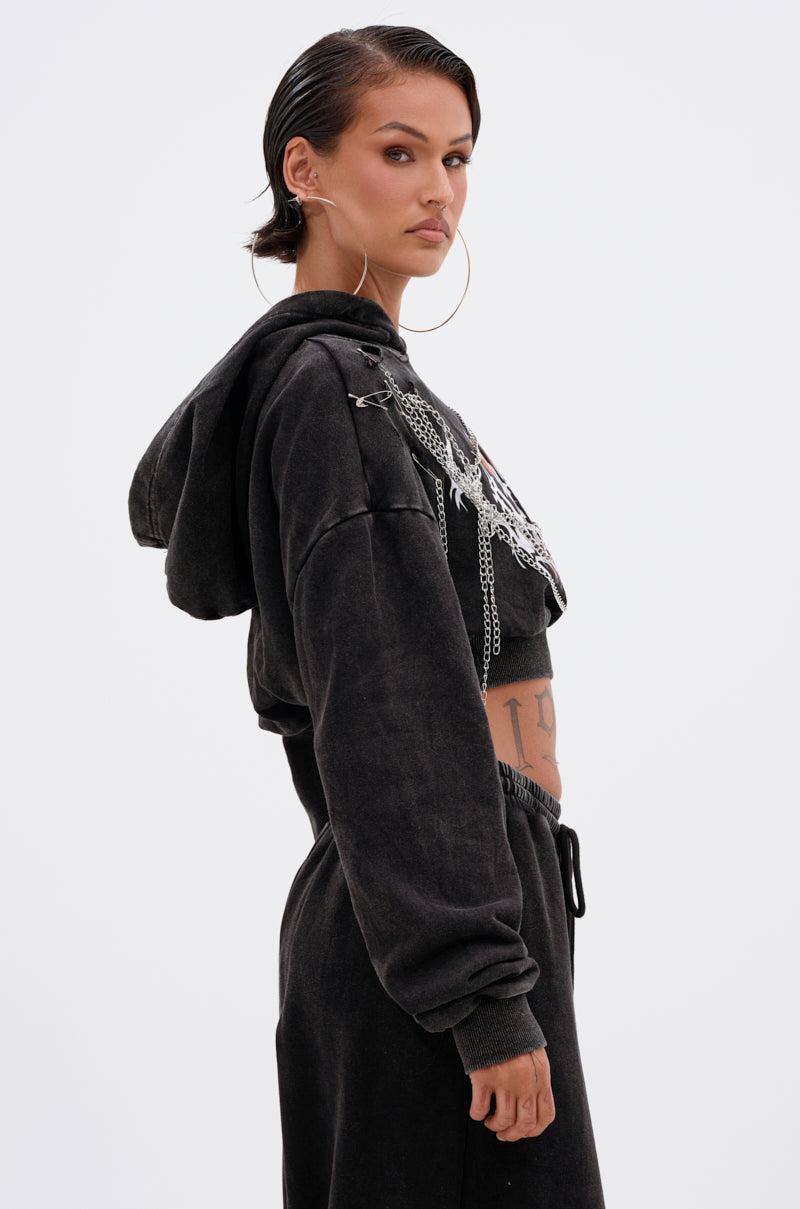 A woman with slicked-back hair and large hoop earrings models the LUCKY ELEVEN CHAIN CROP SWEATSHIRT and matching sweatpants, standing in profile against a white background, showcasing bold streetwear style. 3