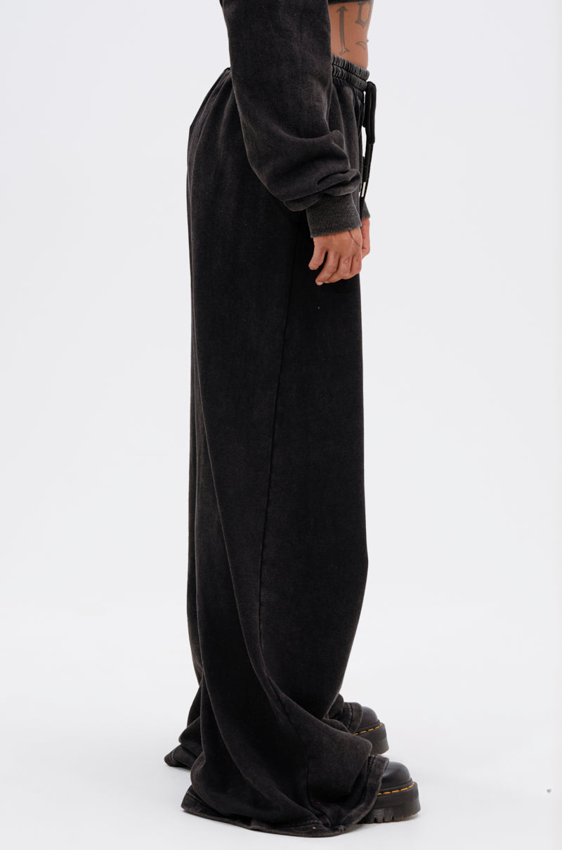 A person stands in profile, wearing LUCKY ELEVEN WIDE LEG JOGGER pants and black platform shoes. Only their lower torso, legs, and one arm are visible against a plain white background. 3
