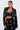 A woman with slicked-back hair wears the OLD FLAME EMBELLISHED BLAZER IN BLACK over a black lace bralette, standing confidently against a plain white background and looking directly at the camera.