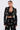 A woman stands against a plain background wearing the OLD FLAME EMBELLISHED BLAZER IN BLACK with faux pearl details, paired with matching high-waisted pants and a black lace bralette visible beneath her blazer. Her hair is pulled back for a chic look.