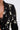 Close-up of a person wearing the OLD FLAME EMBELLISHED BLAZER IN BLACK, adorned with clusters of white pearls in various sizes and paired with a black lace top against a plain, light background.
