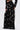 A person in the OLD FLAME EMBELLISHED TROUSER IN BLACK—high-rise, wide-leg pants with faux pearl details—paired with a matching long-sleeve top, stands against a plain light background.