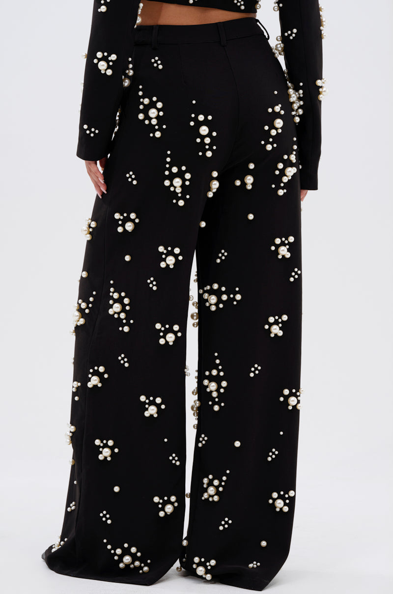 A person is shown from the back against a white background wearing the OLD FLAME EMBELLISHED TROUSER IN BLACK, featuring high-rise, wide-leg design with faux pearl details.