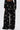 A person is shown from the back against a white background wearing the OLD FLAME EMBELLISHED TROUSER IN BLACK, featuring high-rise, wide-leg design with faux pearl details.