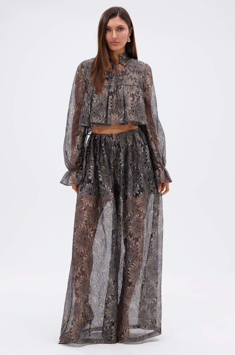 A woman poses against a plain background wearing the BEST GUEST LACE CROP BLOUSE, featuring sheer navy floral lace with long sleeves, paired with matching high-waisted wide-leg pants layered over coordinating shorts. 4