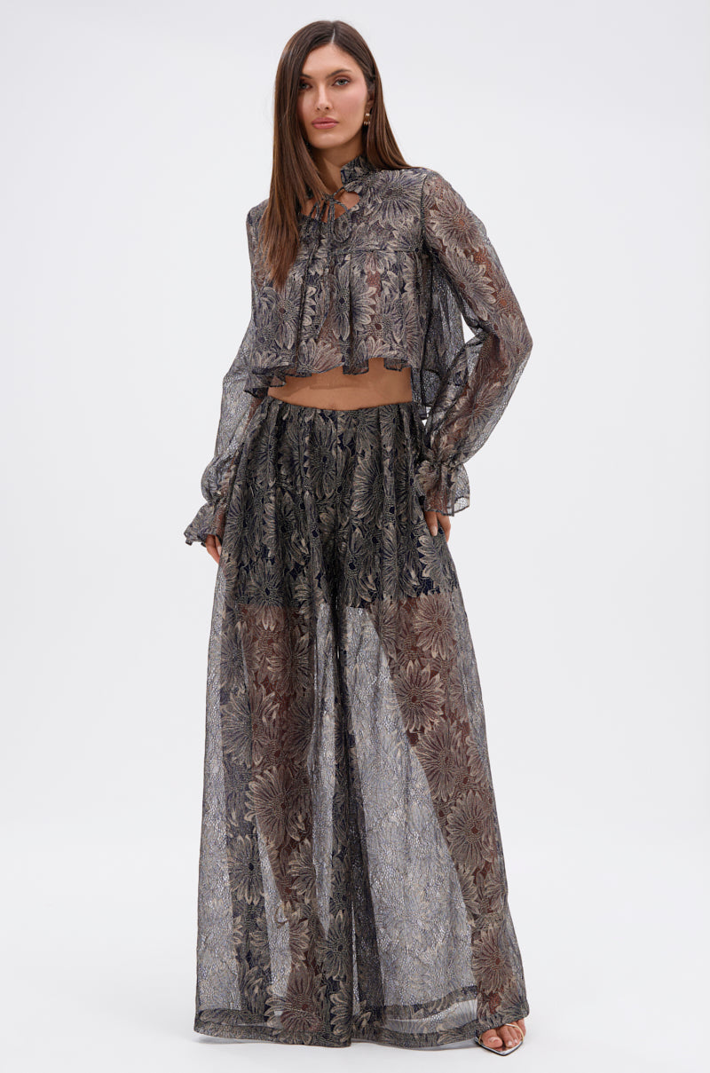 A woman wears the BEST GUEST LACE CROP BLOUSE, a sheer navy, long-sleeved floral blouse paired with matching wide-leg pants. The semi-transparent set features dark and light tones as she faces forward against a plain white background. 5