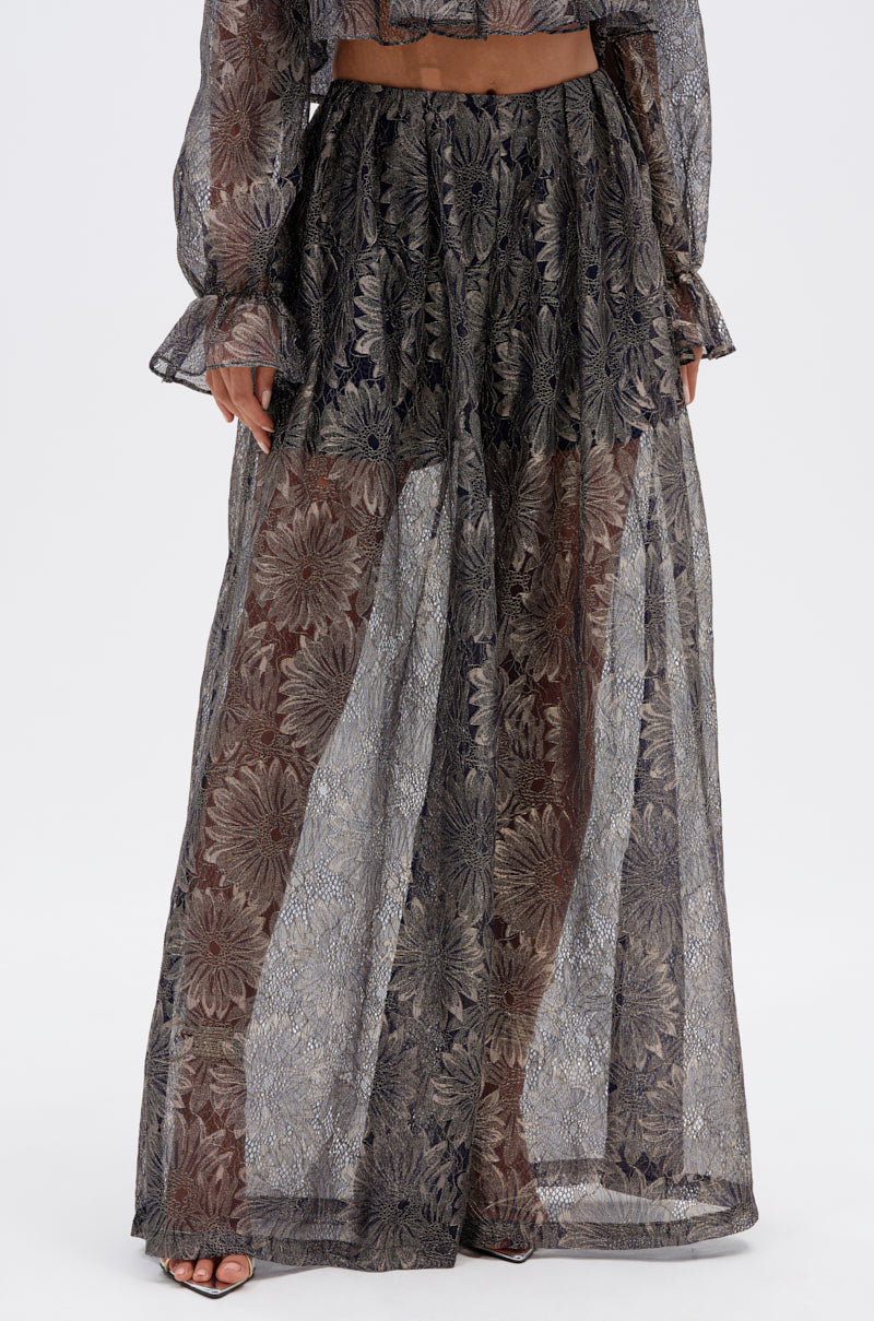 A person wearing the BEST GUEST LACE PALAZZO PANT, featuring a sheer, high-waisted design with metallic floral overlay in black, silver, and gold, paired with a matching long-sleeve top for an elegantly sophisticated look.