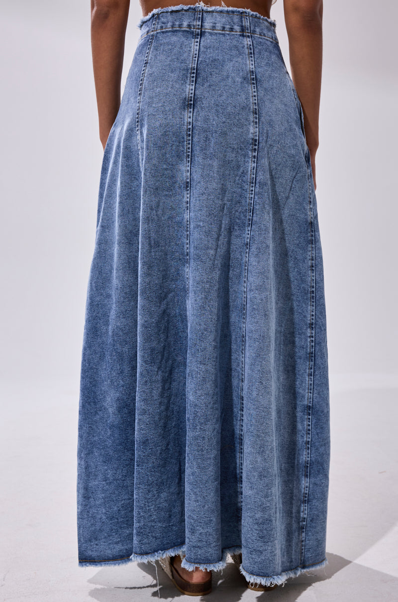 A person stands with their back to the camera against a plain light background, wearing the TIFFANY BLUE DENIM MAXI SKIRT featuring a high-rise fit, visible seams, and a frayed hem.