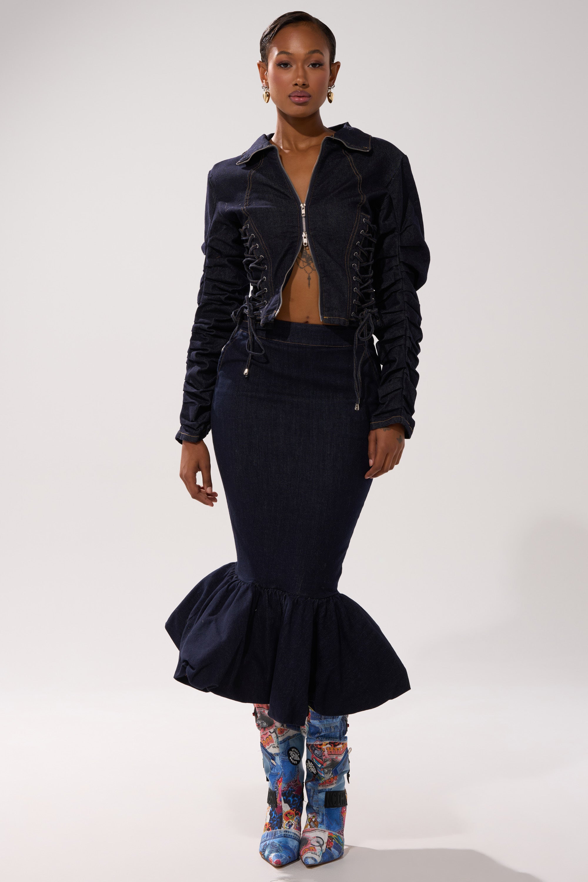 A woman stands confidently facing forward against a plain light background, wearing the STRICTLY BUSINESS DENIM BLOUSE with ruched sleeves, paired with a matching high-waisted mermaid skirt and colorful floral boots.