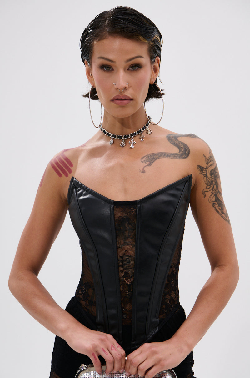 A person with short dark hair and hoop earrings wears the TOO GOOD FOR THIS LACE CORSET with sheer floral lace, displaying tattoos—including a dragon on their shoulder—and a choker, standing against a plain white background.