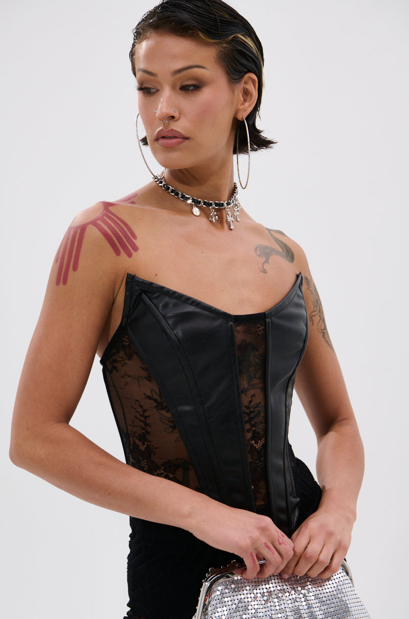A person with short dark hair and hoop earrings wears the TOO GOOD FOR THIS LACE CORSET, a layered necklace, and holds a silver sequined bag. They have a pink handprint tattoo on their shoulder.