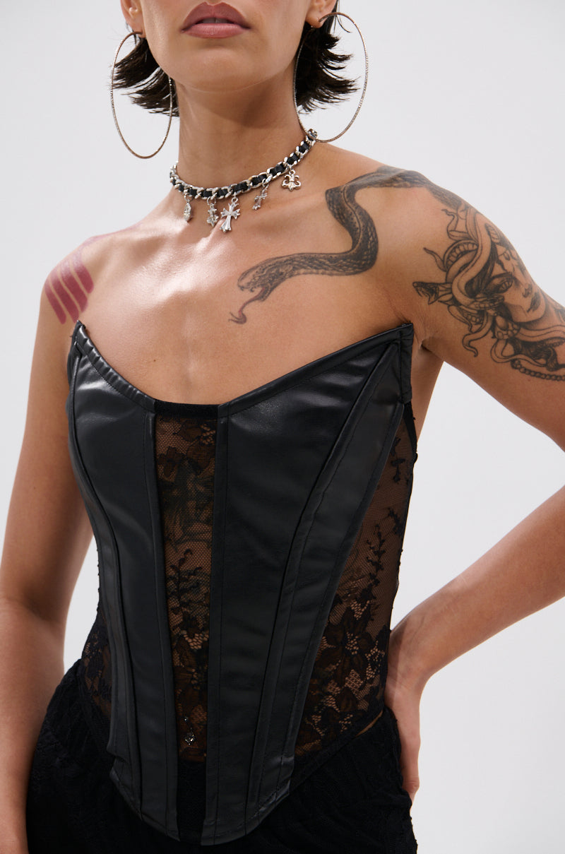A person wearing the TOO GOOD FOR THIS LACE CORSET, featuring black lace and faux leather panels, styled with hoop earrings and a black charm choker. Tattoos of a snake and geometric shapes are visible. Image is cropped at shoulders and waist.