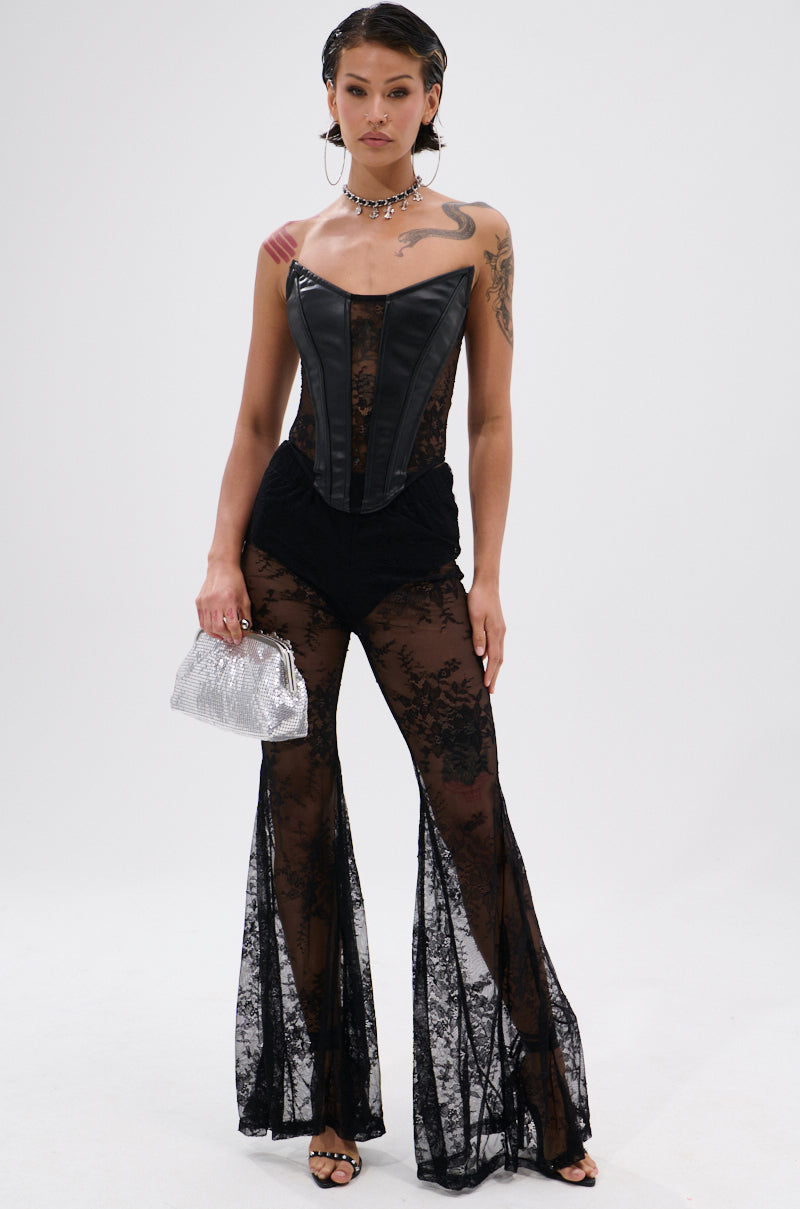A woman stands confidently in the TOO GOOD FOR THIS LACE FLARE LEGGING, paired with a leather corset top. She holds a silver handbag, wears black heels, hoop earrings, and a choker, showing off her arm tattoos against a plain white background.