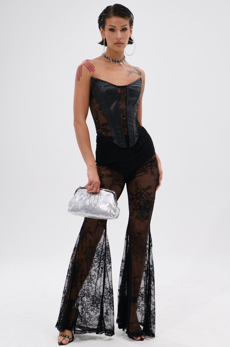 A woman models the TOO GOOD FOR THIS LACE FLARE LEGGING—sheer floral lace bell bottom leggings—with a strapless black leather corset, silver glitter purse, hoop earrings, choker necklace, and black heels against a plain white background.